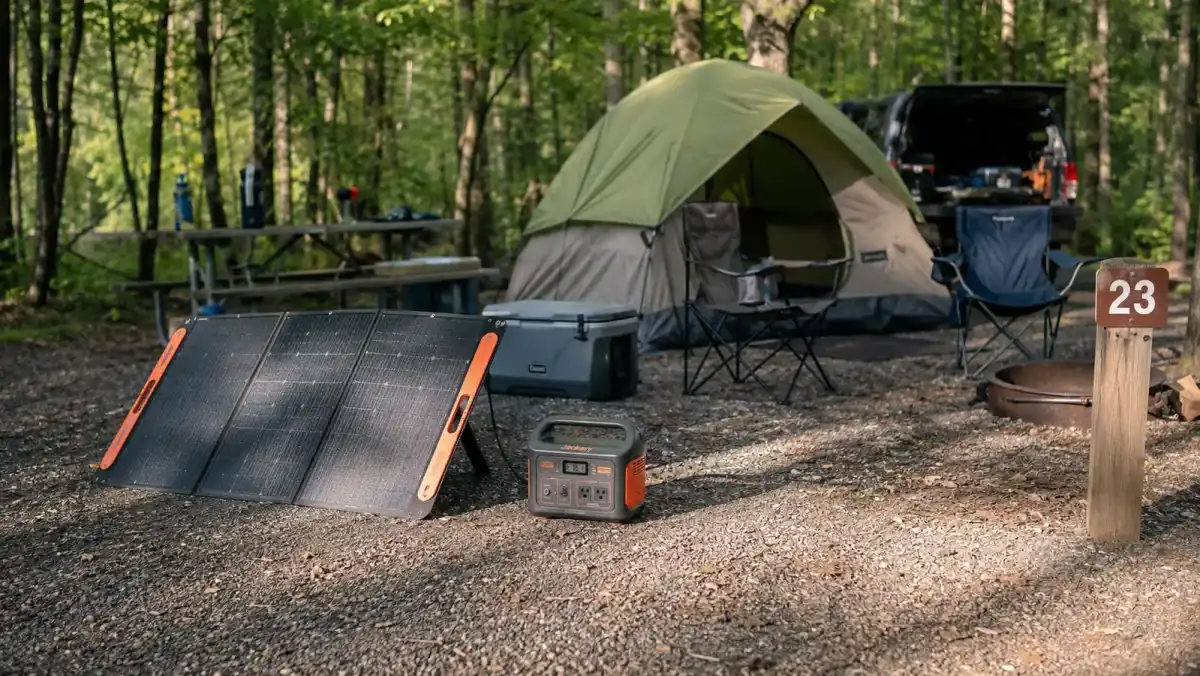 Portable power station charging from a small solar panel set up outside a tent at a campground