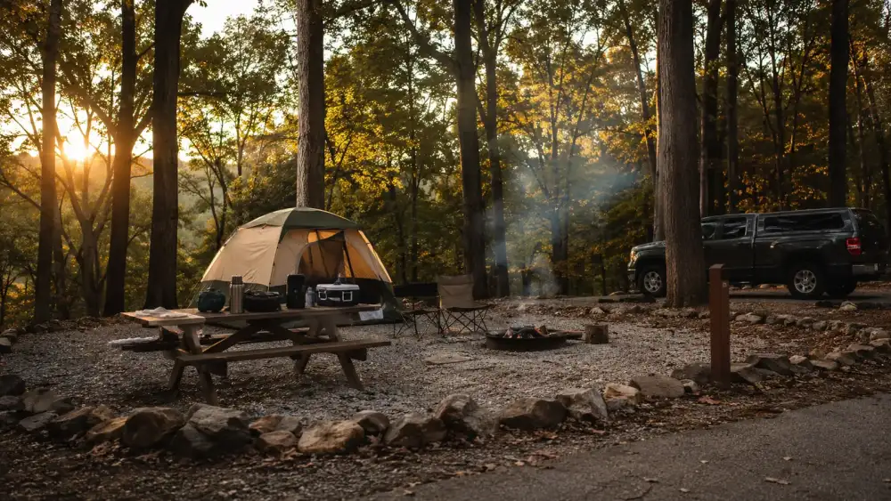 A quiet campsite at dusk with a pitched tent, a folding camp chair, and a lantern glowing on the picnic table
