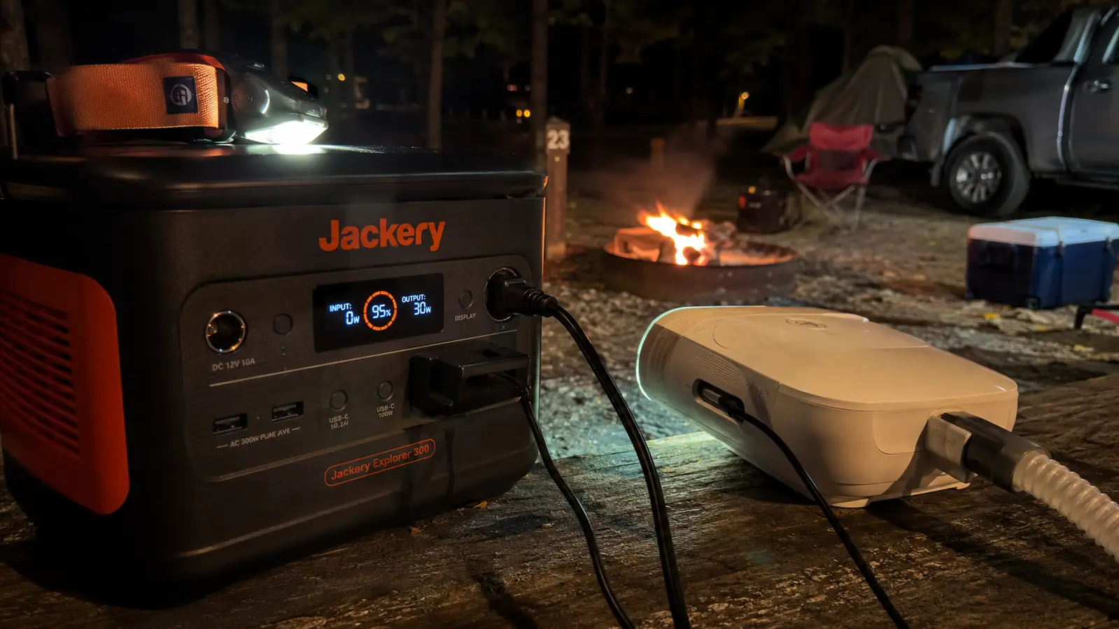 Close-up of a CPAP machine plugged into the AC outlet of a portable power station on a picnic table at night