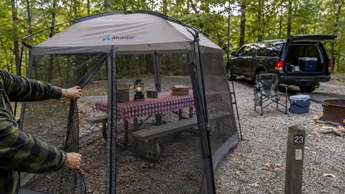 Hand unzipping the mesh door of the Alvantor screen house canopy to step inside at a campsite