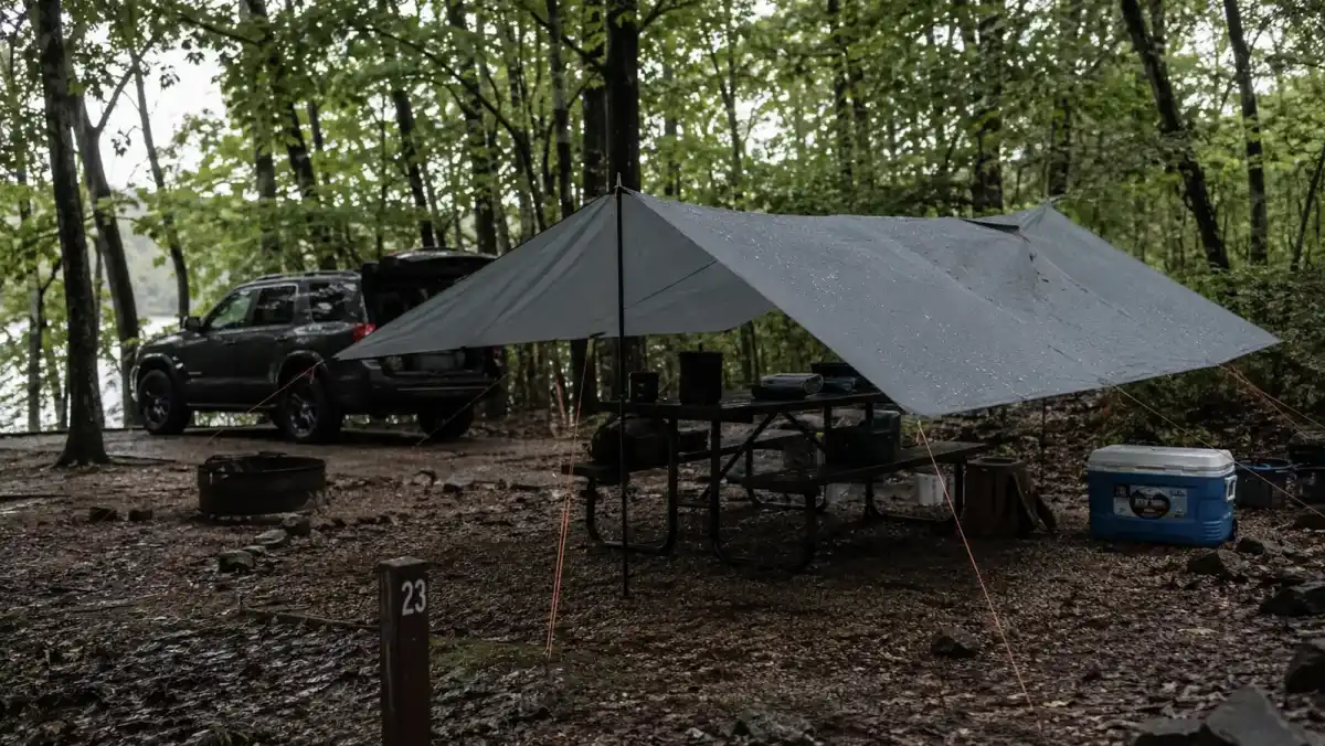 A basic dining fly tarp pitched low and taut over a picnic table during a rain shower at a campground